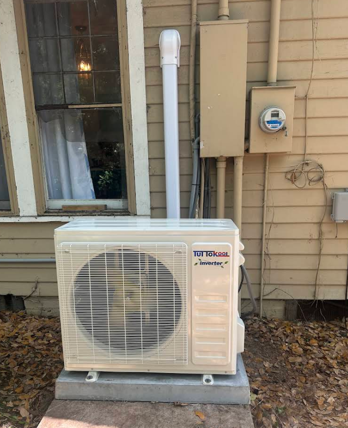 Outdoor HVAC unit next to a window and utility box on the side of a building.