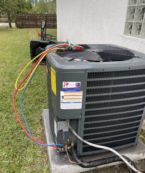 Air conditioning unit with hoses attached, outdoors, near a building.