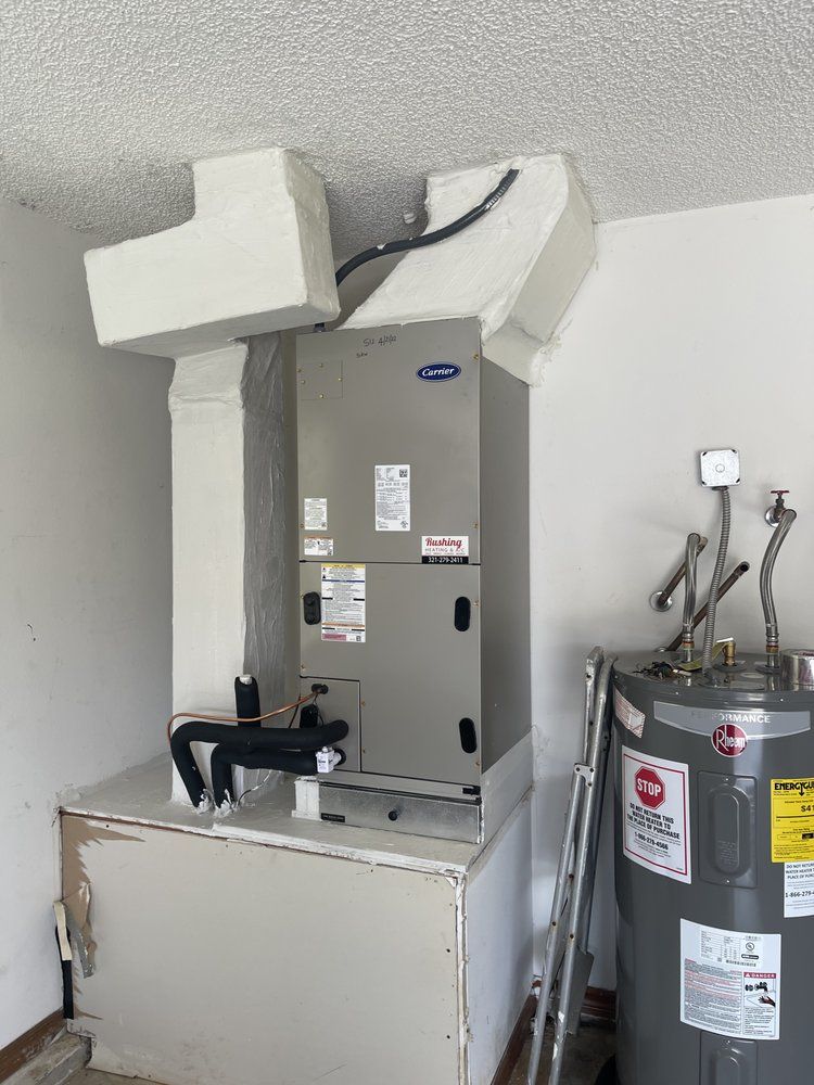 HVAC unit and water heater in a garage. Unit is mounted on a platform, ductwork above.