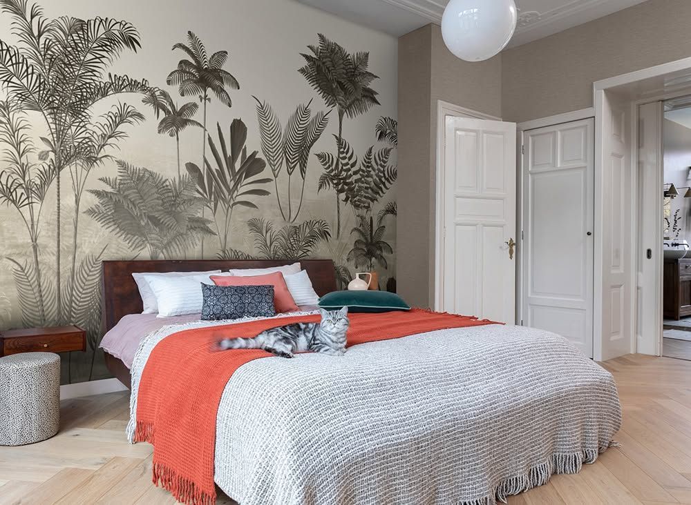 Camera da letto luminosa con carta da parati tropicale, letto rifatto e lenzuola arancioni .