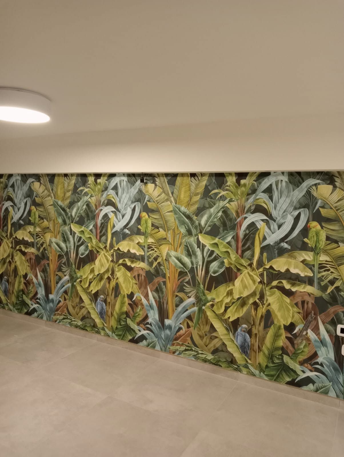 Murale con foglie tropicali su una parete del corridoio, accanto a una lampada da terra e da soffitto beige.