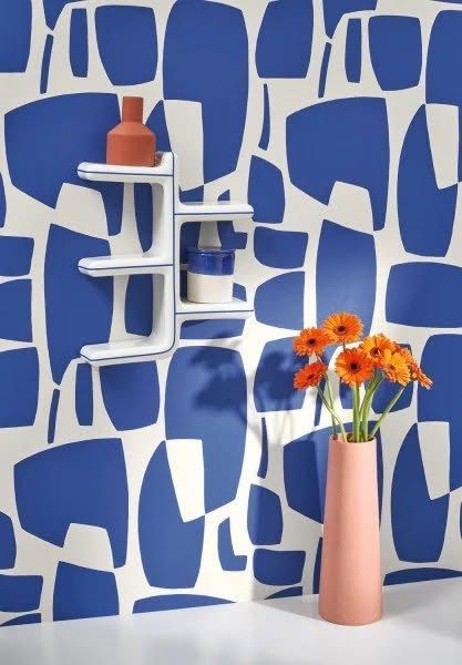 Parete decorata con motivi blu e bianchi, mensola bianca, vaso arancione e vaso di fiori rosa.