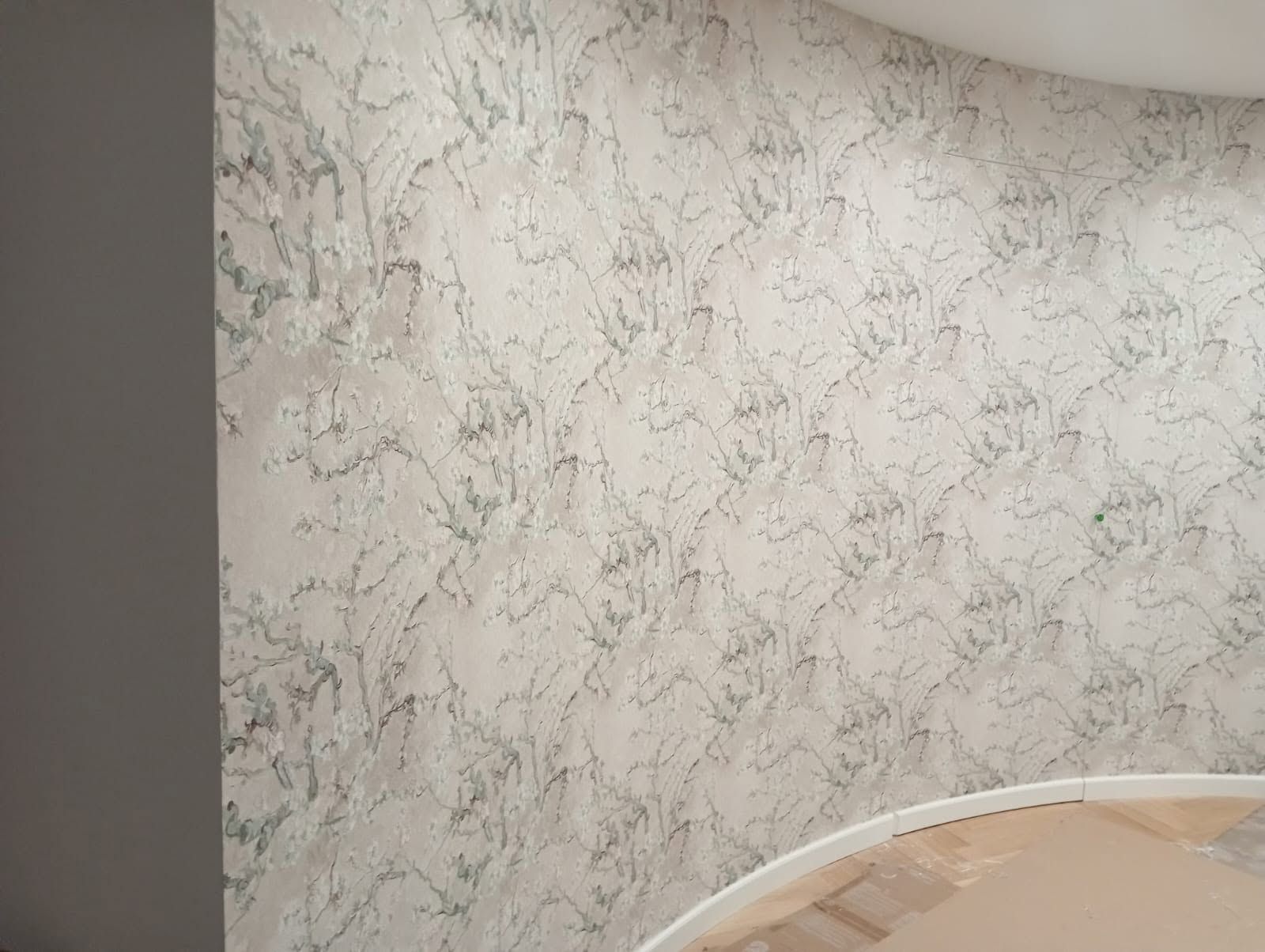 Carta da parati beige a motivi geometrici e il bordo curvo di un letto in una stanza illuminata da una luce soffusa.