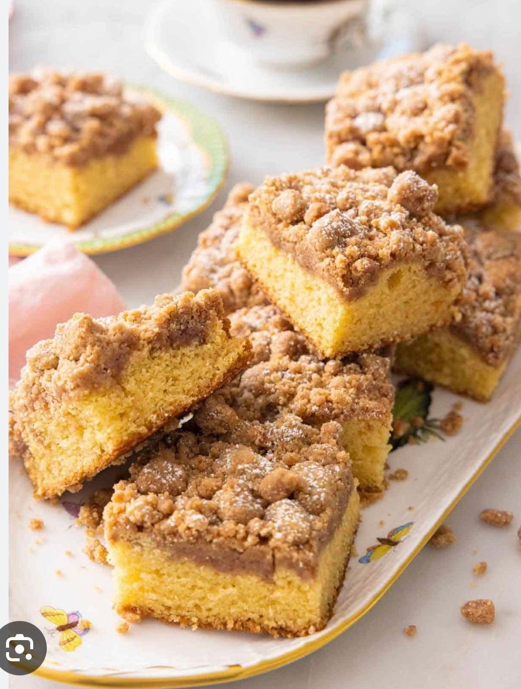 Sliced crumb-topped cake bars on a white platter with a cup and saucer in the background