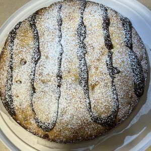 Powdered sugar-dusted round cake on a plate, drizzled with dark chocolate