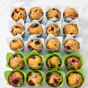 Tray of assorted blueberry muffins in white and green paper liners, viewed from above.