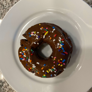 Chocolate-glazed donut with colorful sprinkles on a white plate