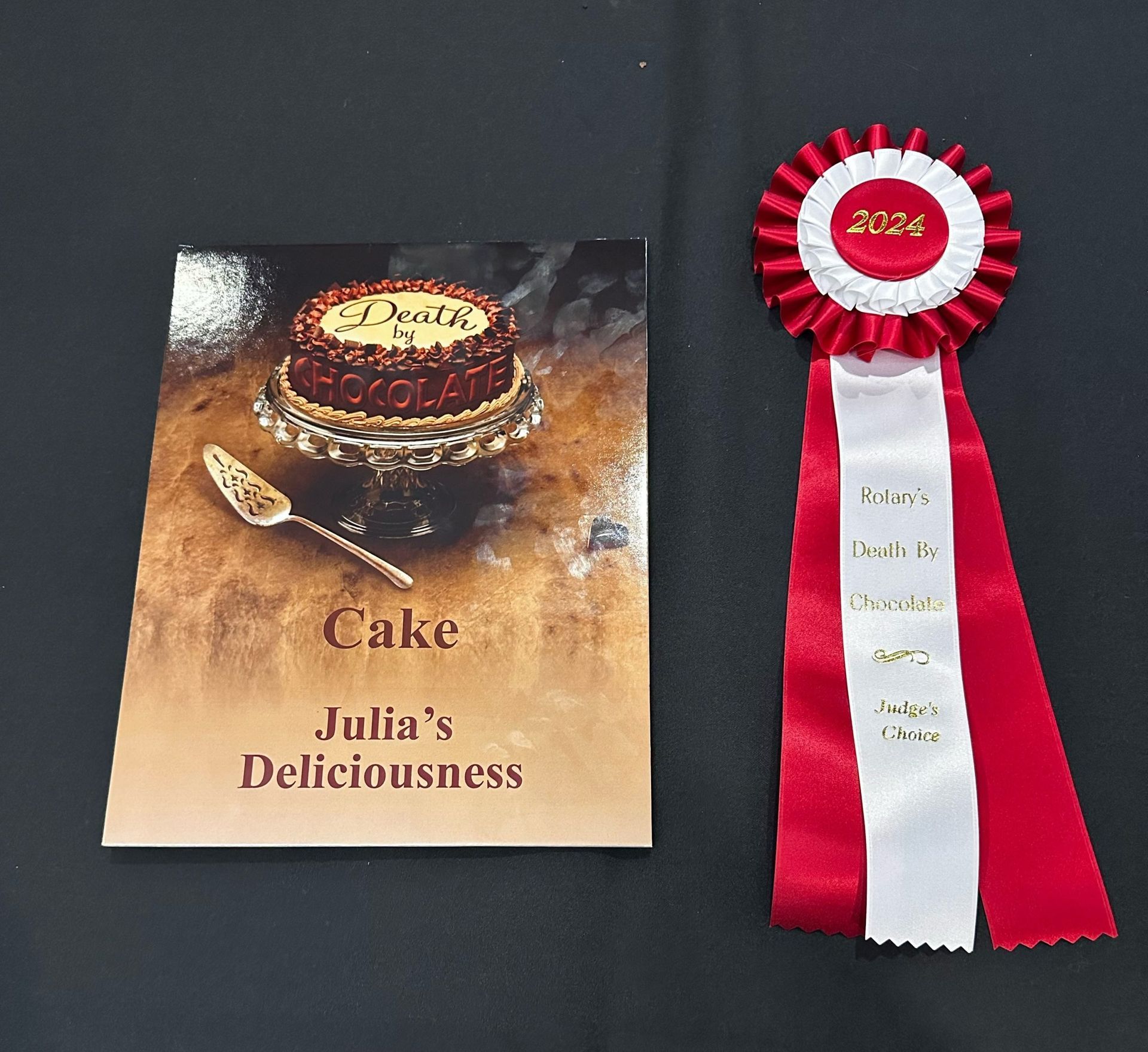 Cake award certificate with red rosette ribbon on a dark background