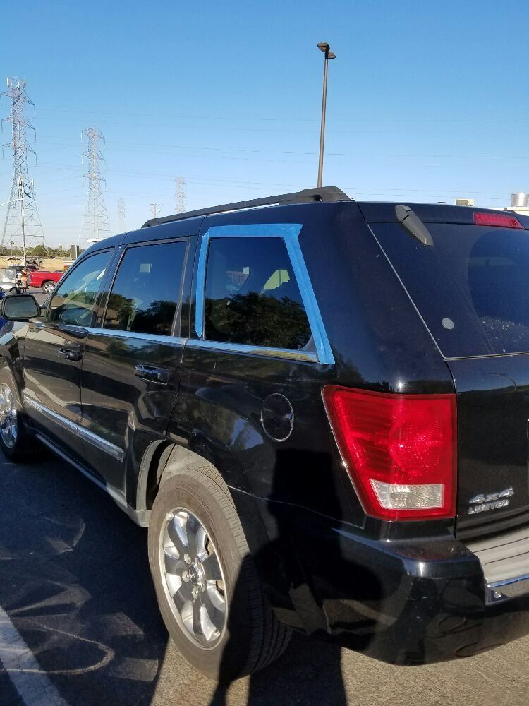 A black jeep with blue tape on the window is parked in a parking lot.
