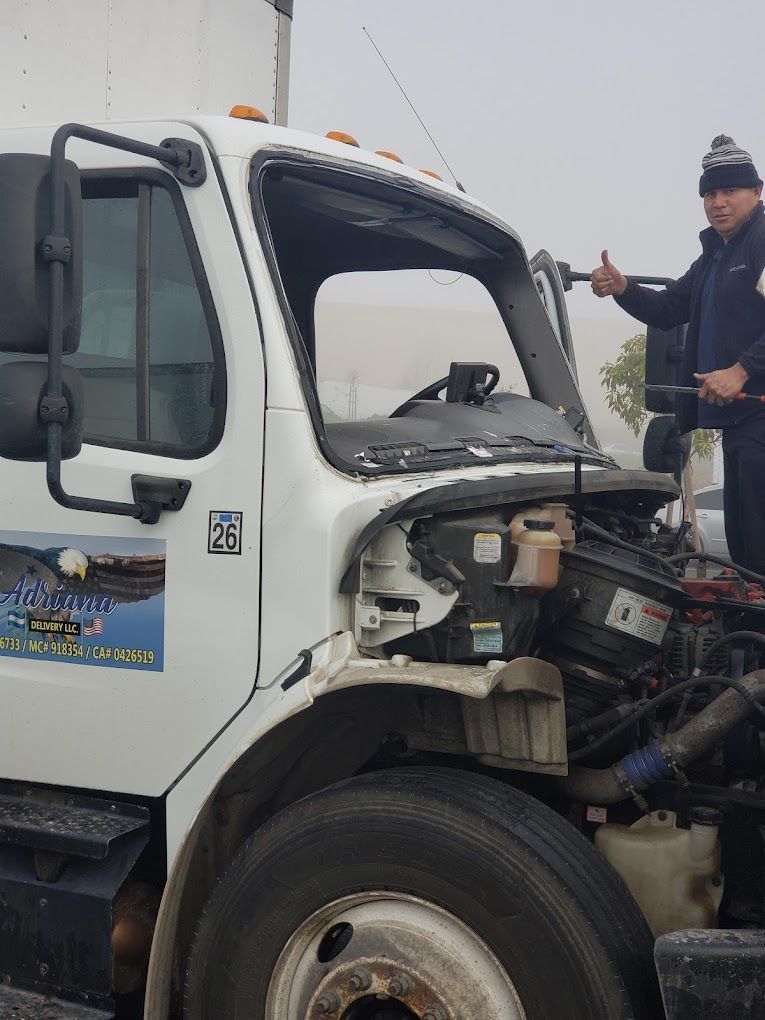 Two men are working on a white truck with the hood open