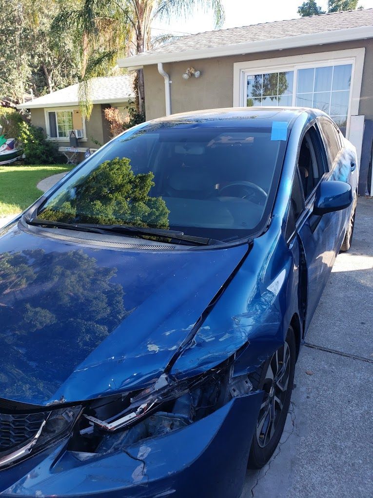 A blue car with a broken windshield is parked in front of a house.