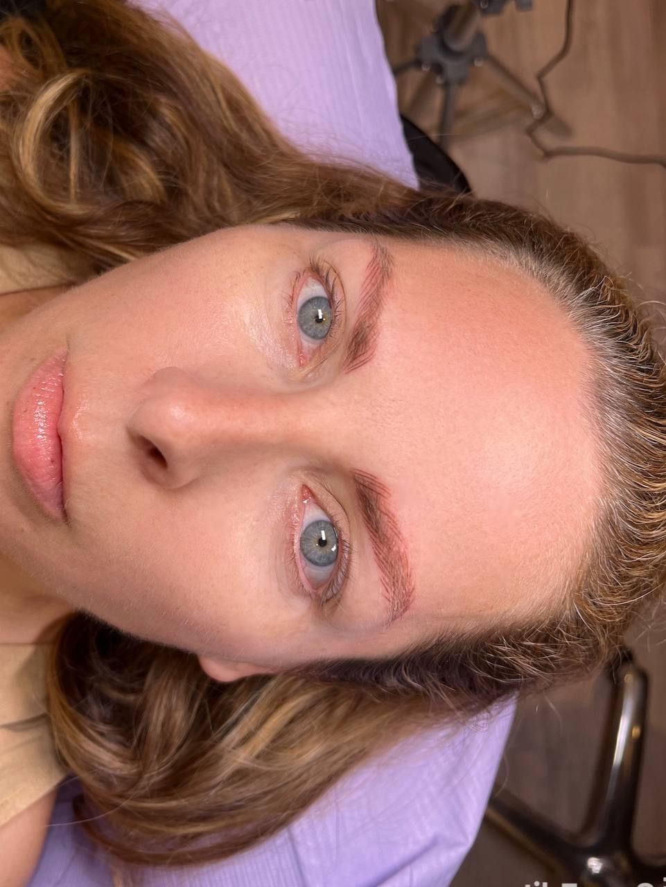 Woman with light skin, blue eyes, recently tattooed eyebrows, lying down.