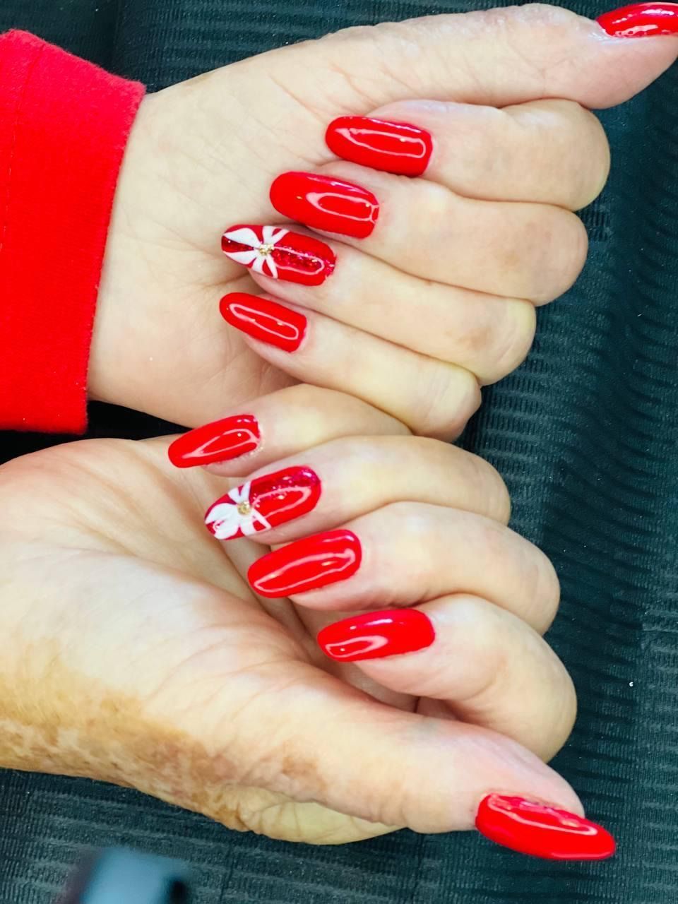 A close up of a woman 's red nails with a white flower design