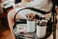 Makeup brushes in white containers on a tray; person in background, getting ready.