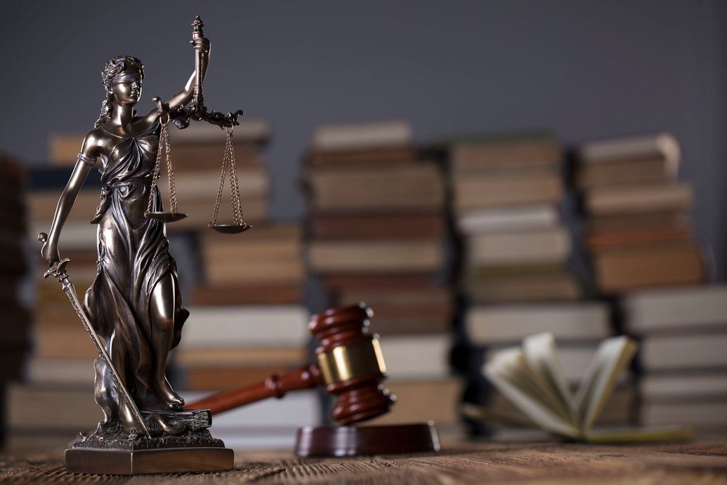 Una estatua de la justicia está sentada en una mesa de madera al lado de un mazo de madera.