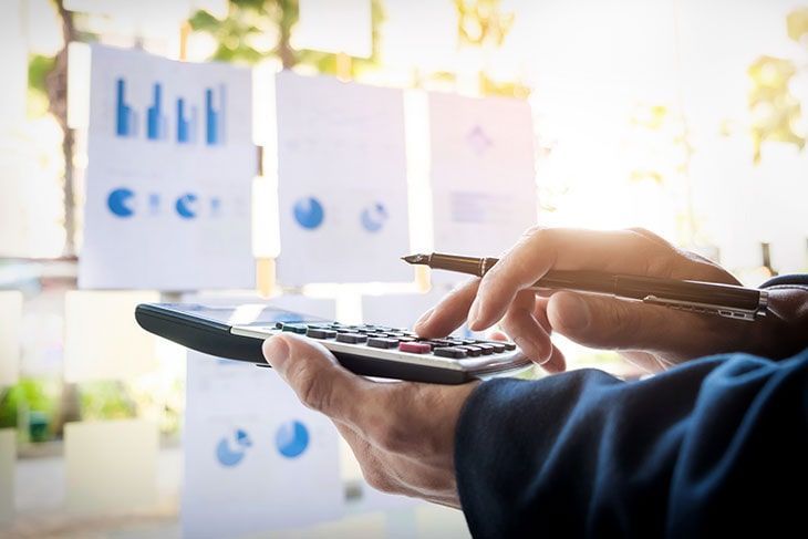 Persona que utiliza una calculadora con gráficos en el fondo, iluminada por la luz del sol.