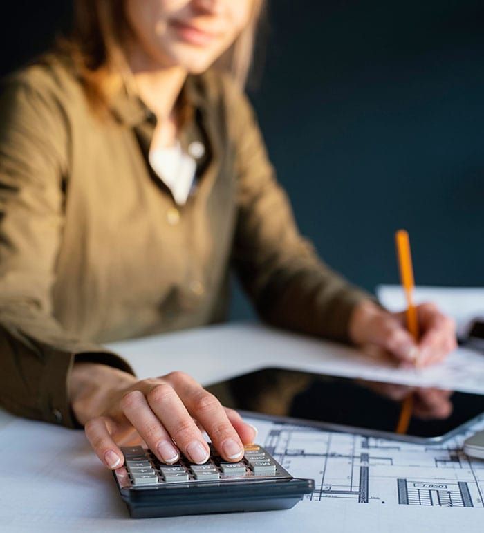 Mujer usando una calculadora, escribiendo con un lápiz, trabajando en planos en una mesa.