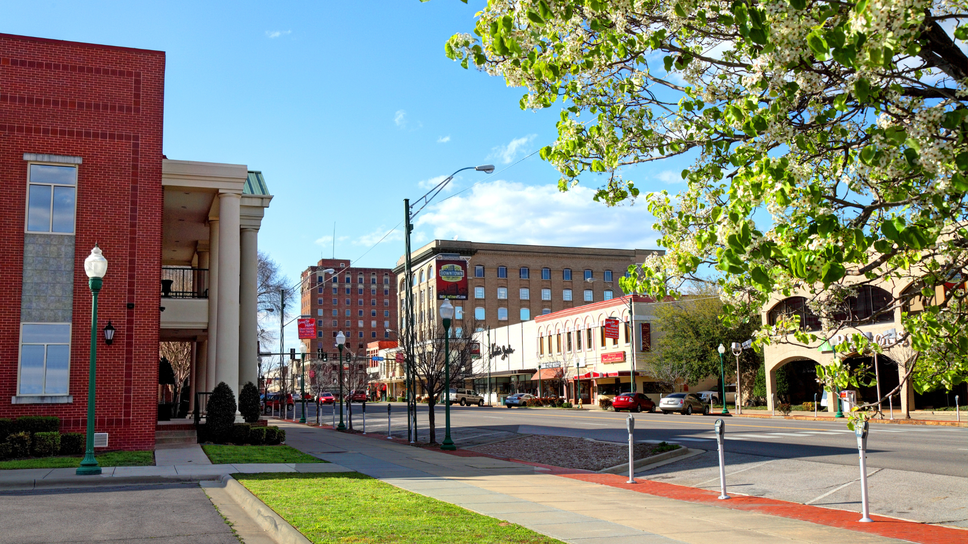 Street view of buildings in downtown, brick and cream facades, street with cars, bright day.