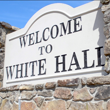 A stone wall with a sign that says welcome to white hall, AR