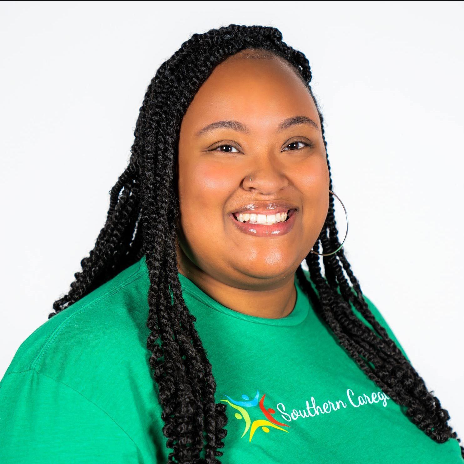 Smiling person in a green shirt with long braids against a white background