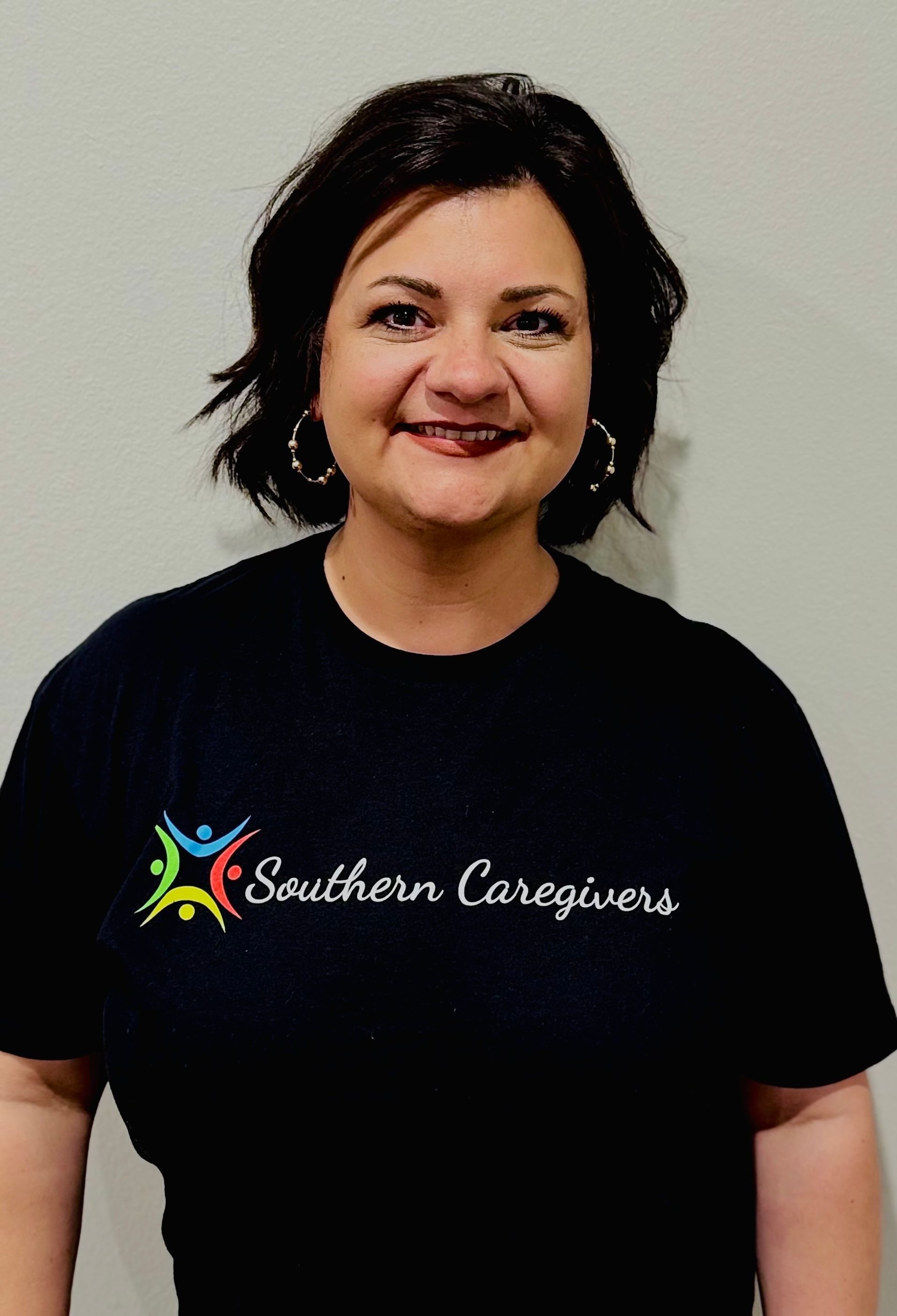 Smiling person in a black Southern Caregivers T-shirt standing against a plain light wall
