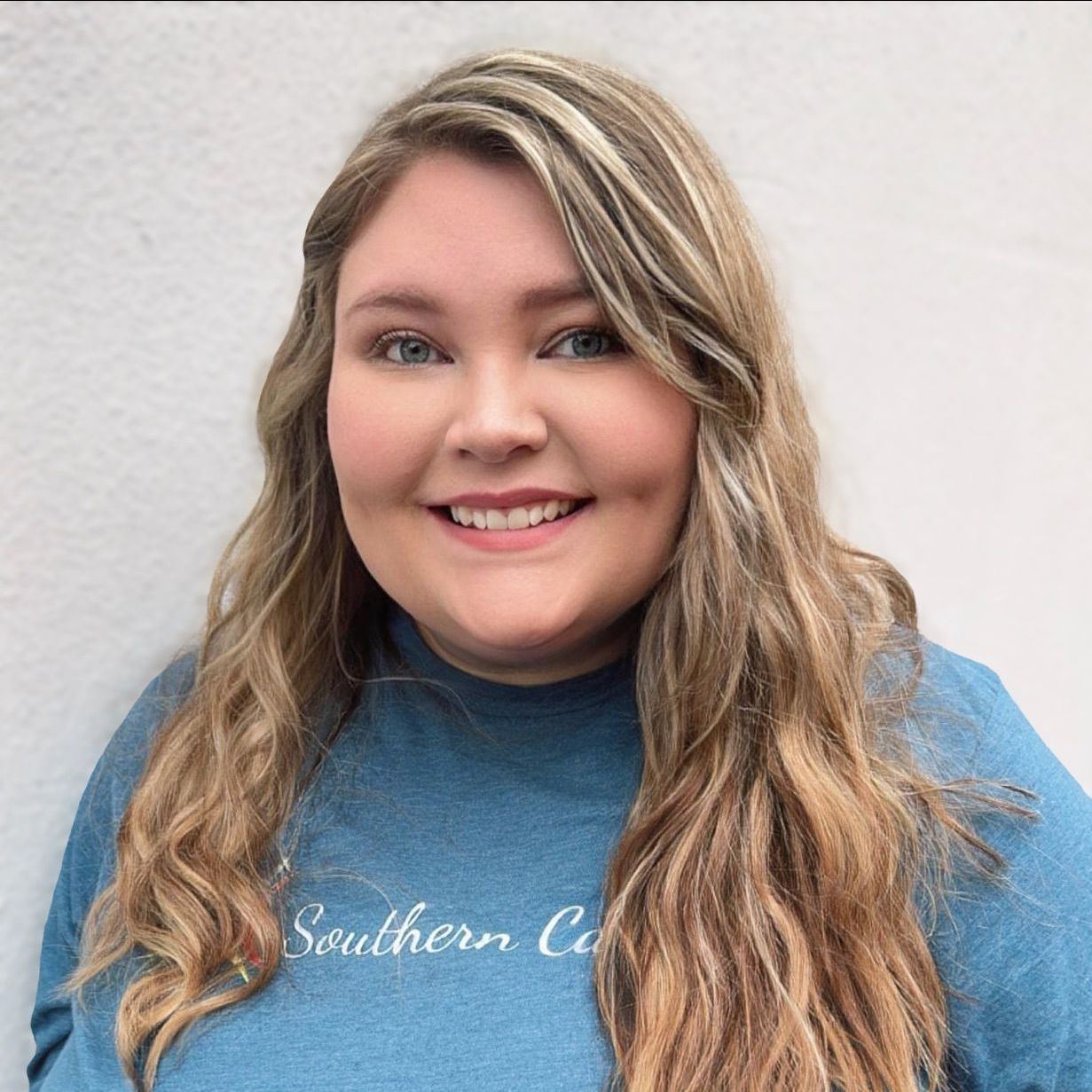 Smiling person in a blue shirt standing against a light wall