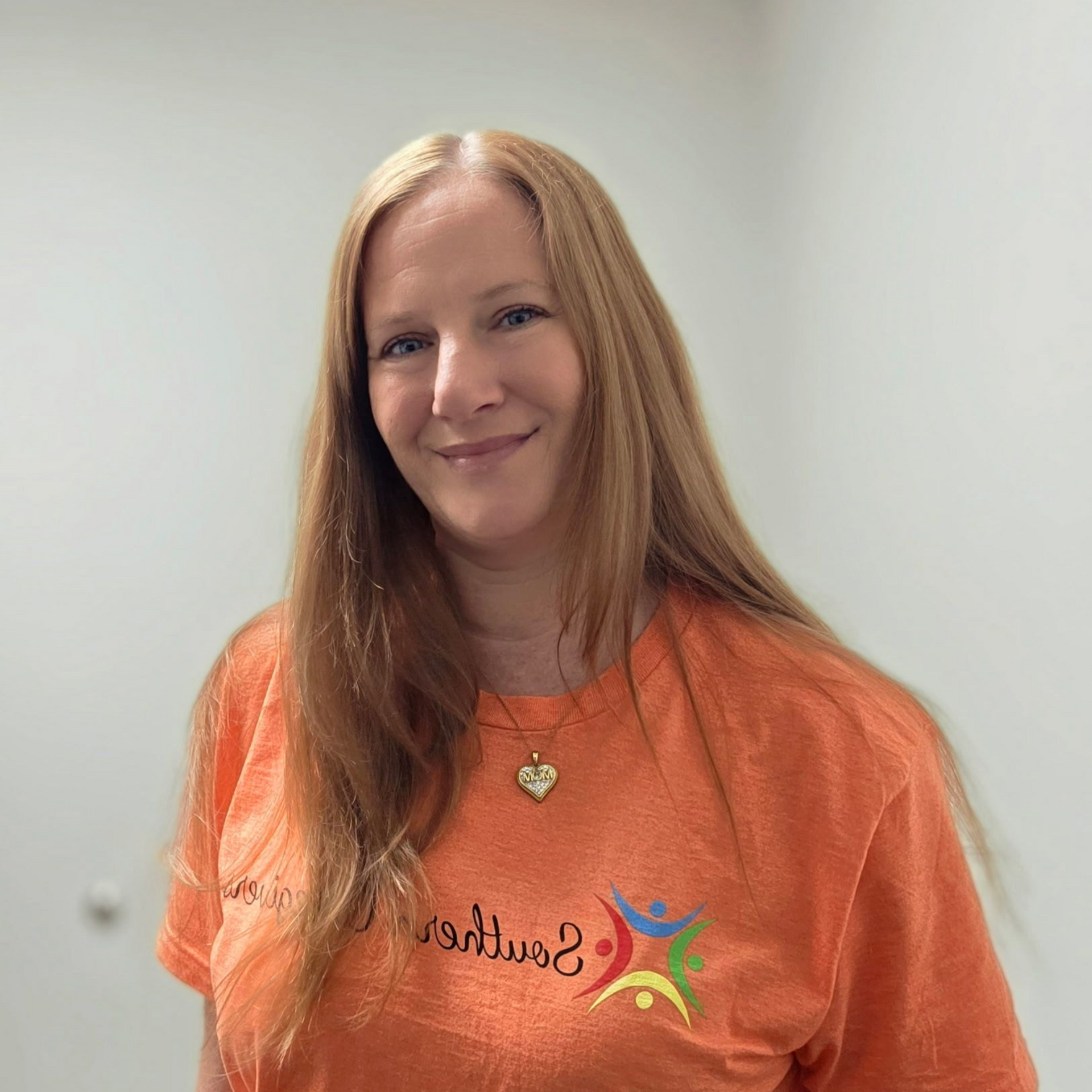 Woman with long red hair smiling in an orange shirt against a plain light background