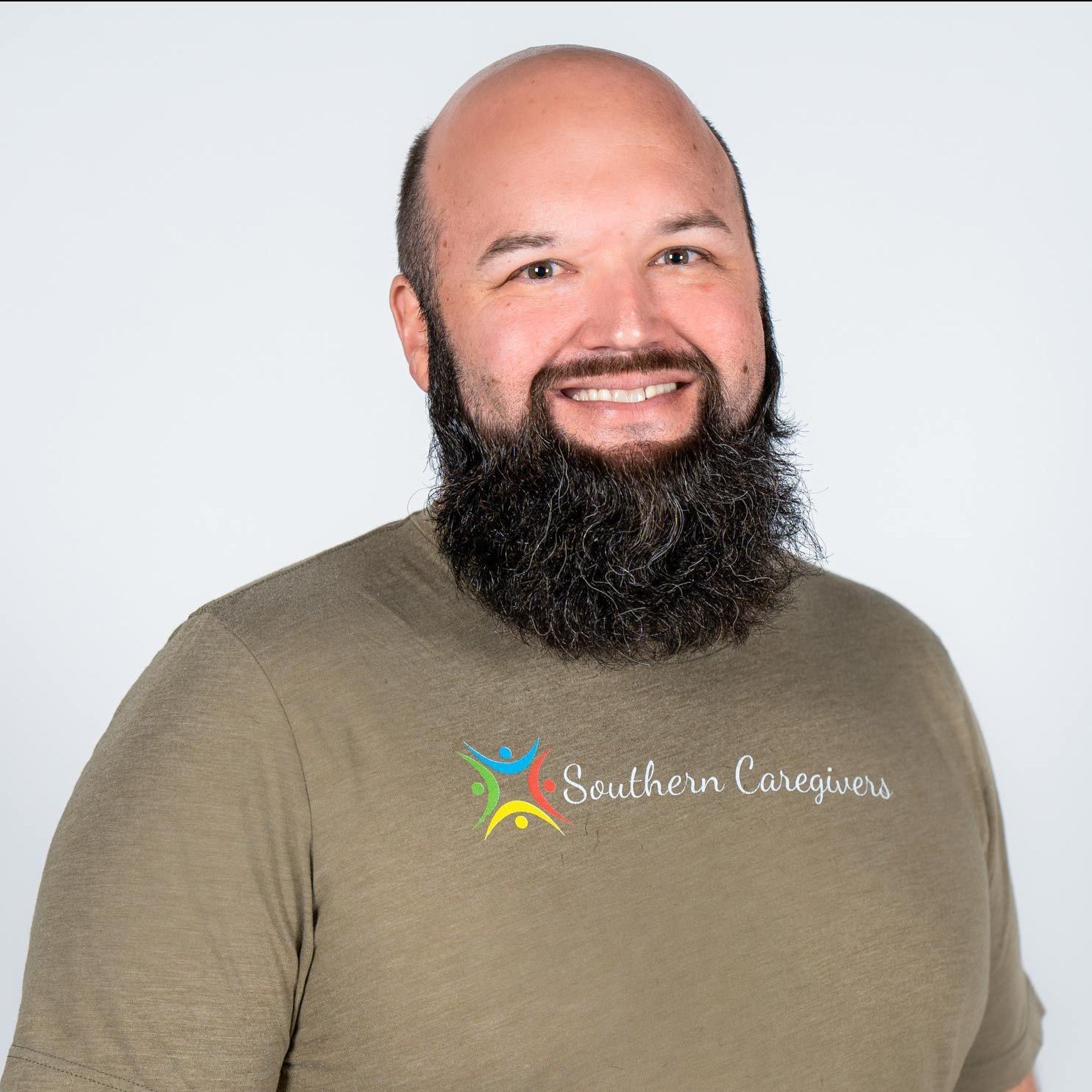 Smiling bald man with a full beard wearing an olive T-shirt against a light background