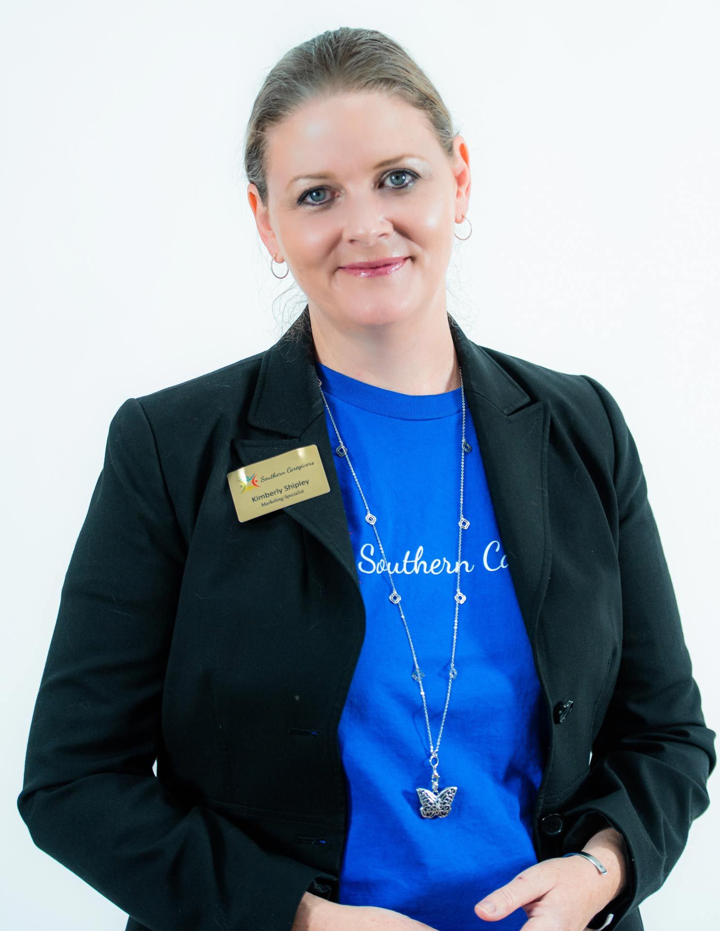 Woman in black blazer and blue shirt, wearing a name badge, against a white background