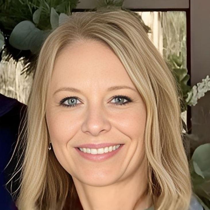 Smiling blonde woman in a bright indoor setting with greenery in the background