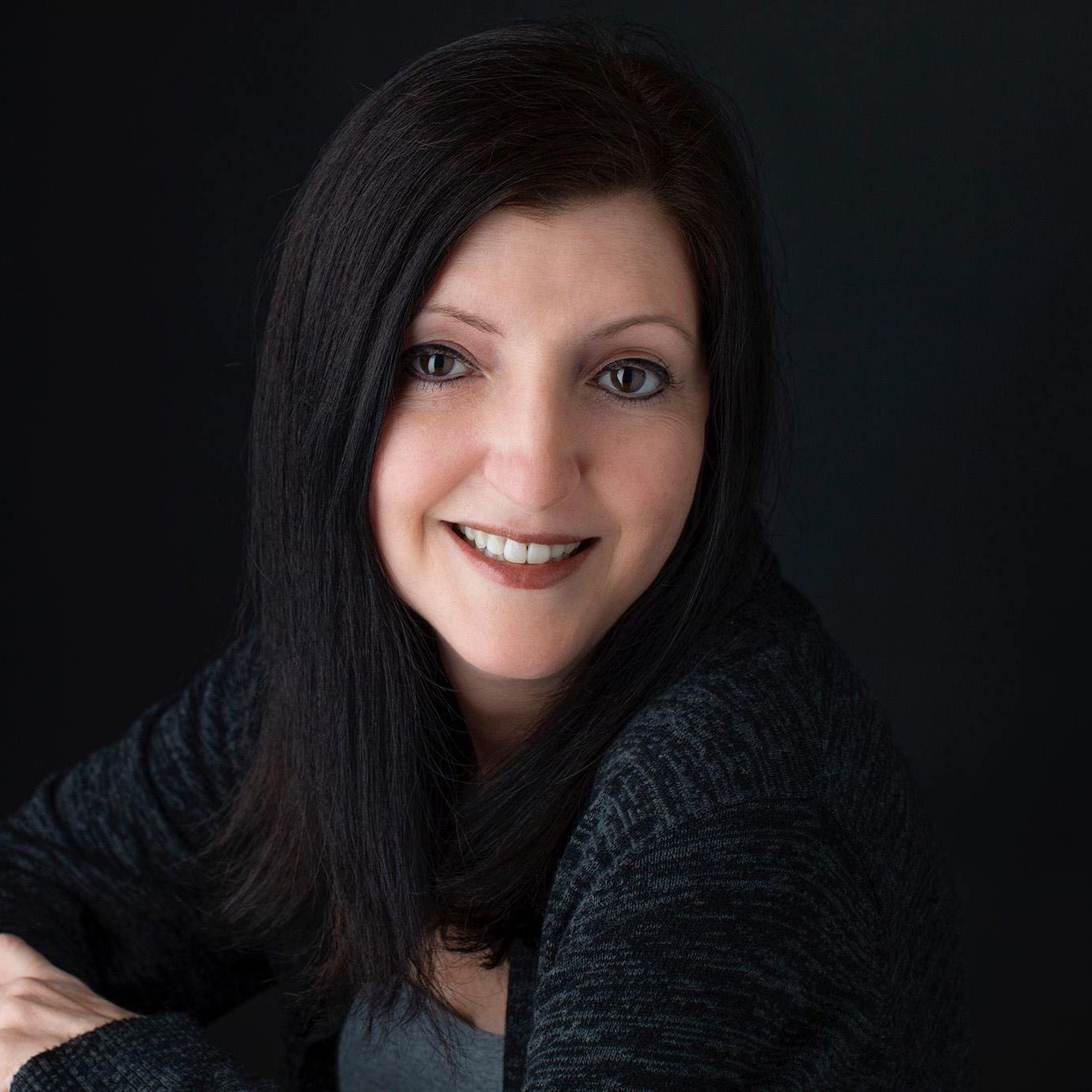 Portrait of a smiling woman with long dark hair against a dark background
