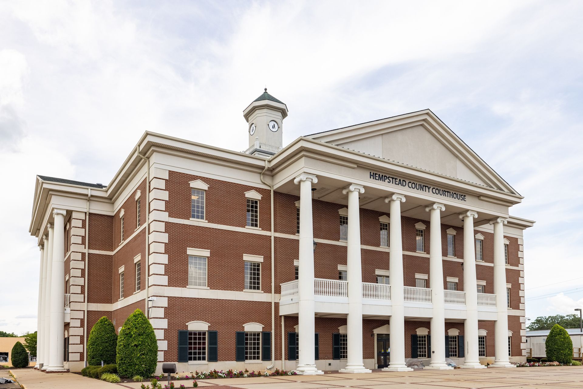 Historic brick courthouse with white columns and a clock tower under a cloudy sky.