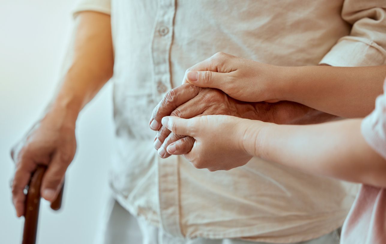 A woman is holding the hand of an elderly man with a cane.