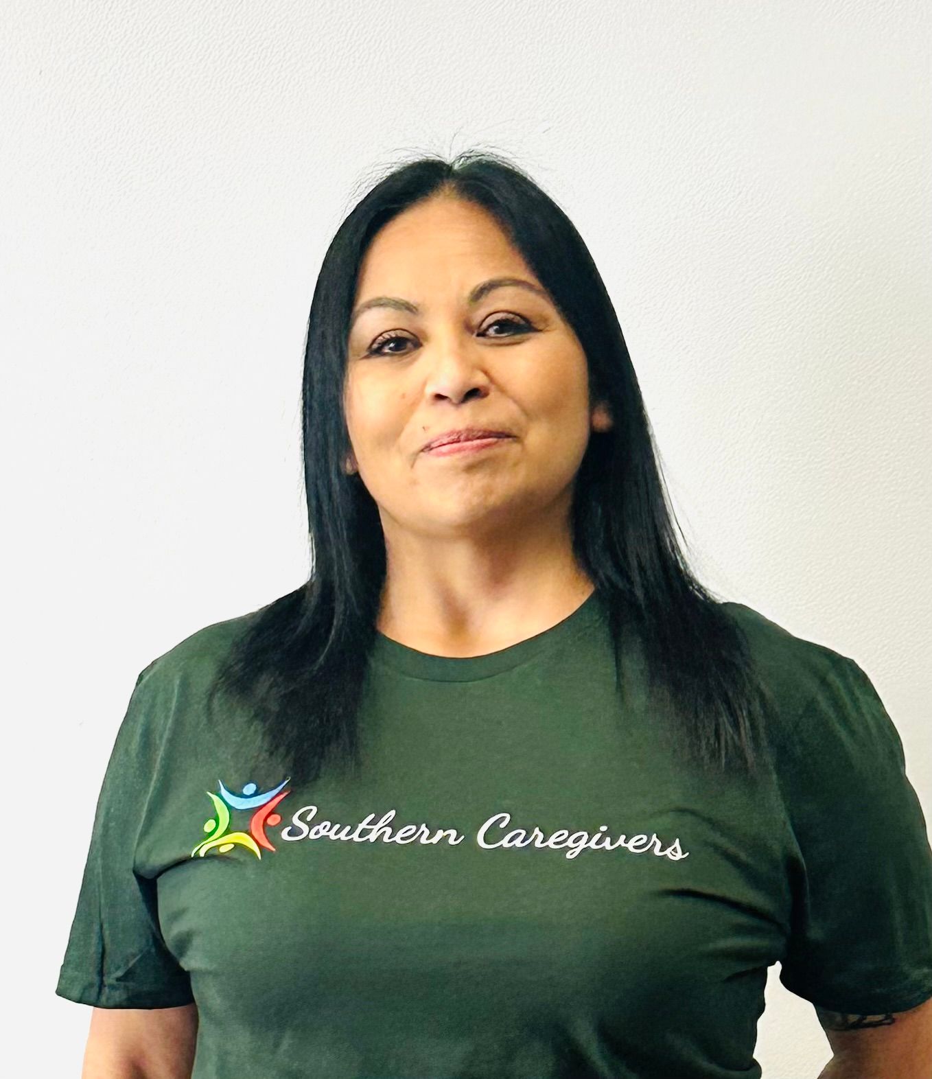 Woman in a green Southern Caregivers T-shirt standing against a plain white wall