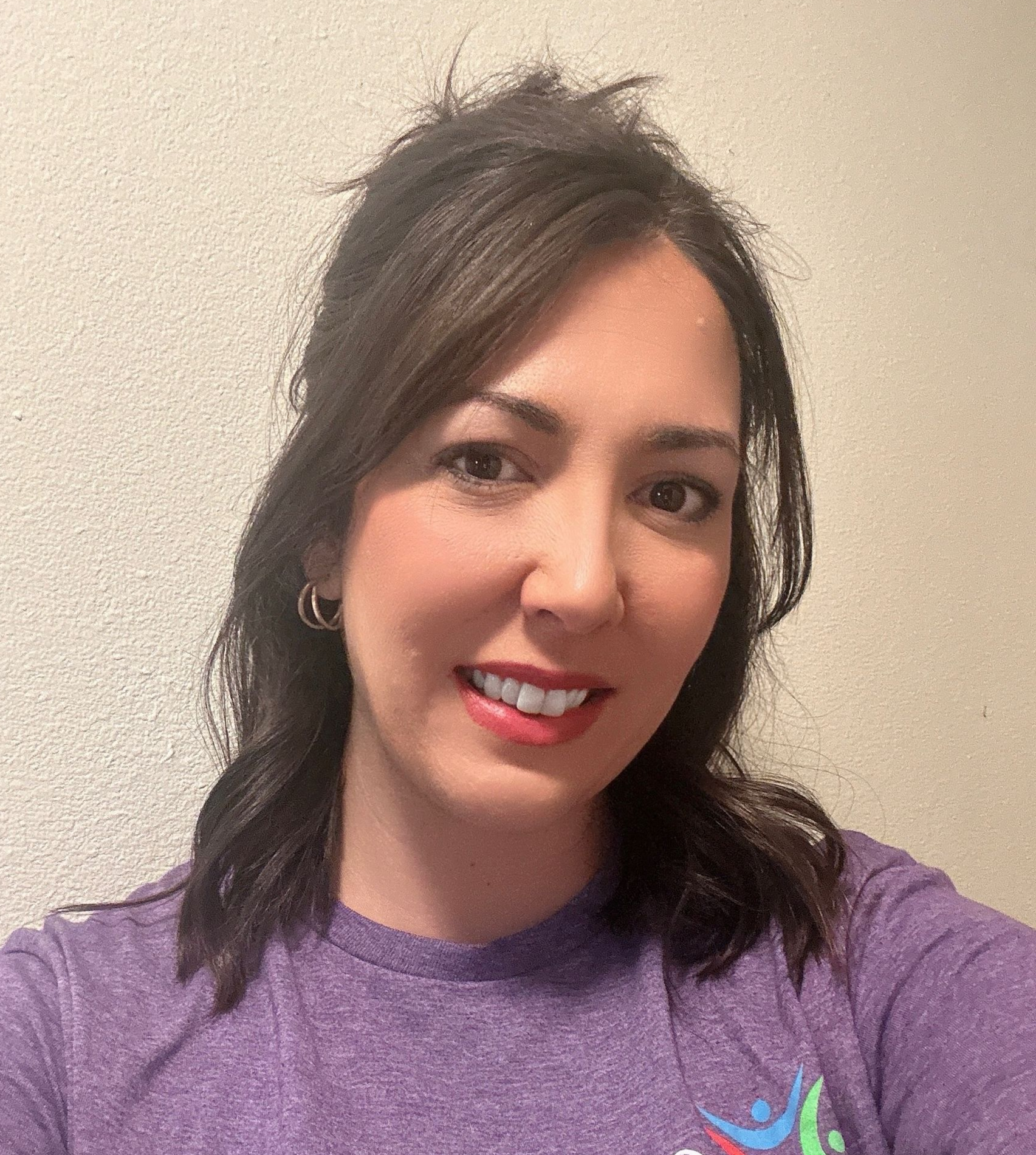 Smiling woman in a purple T-shirt against a beige wall