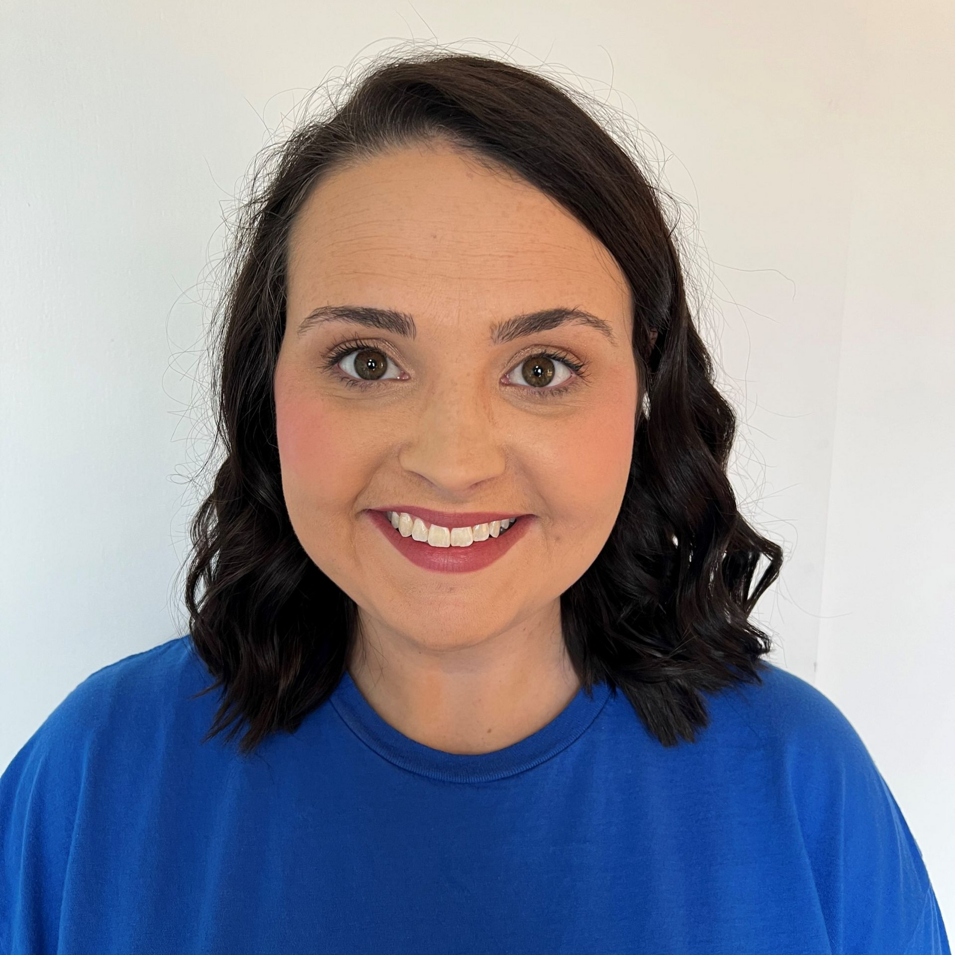 Woman with dark hair smiles, wearing a blue shirt.