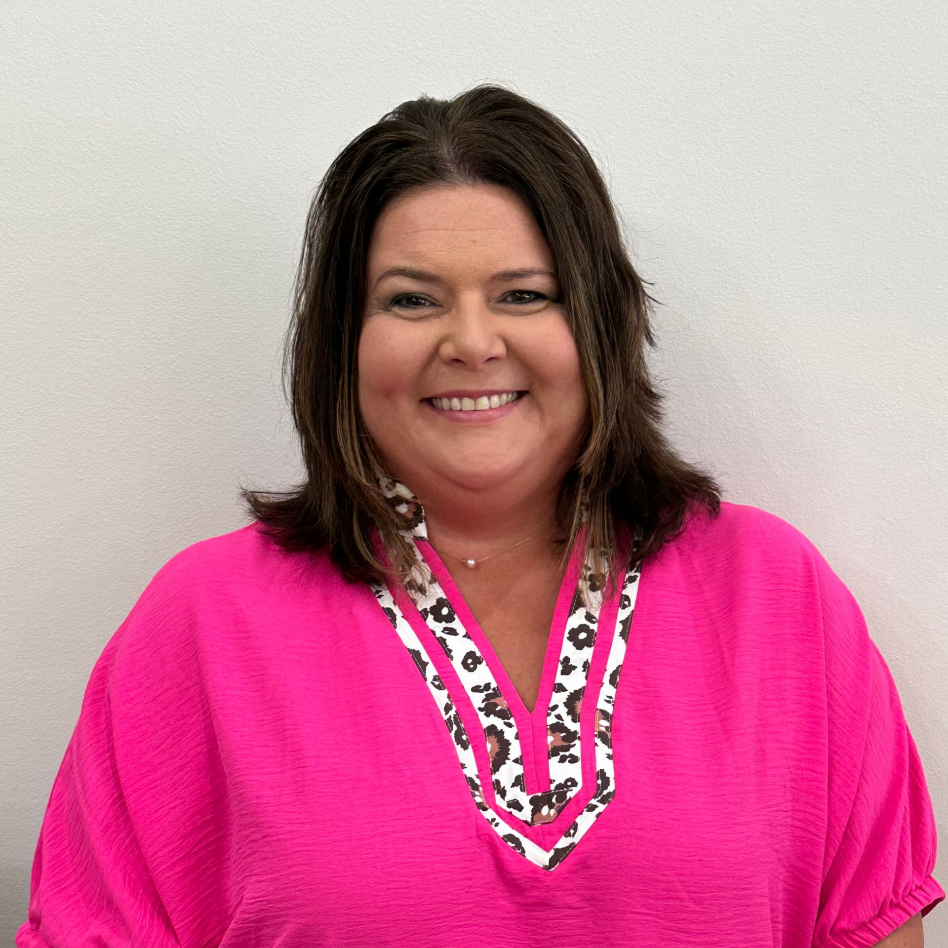 Smiling person in a bright pink top with a patterned neckline against a plain light background