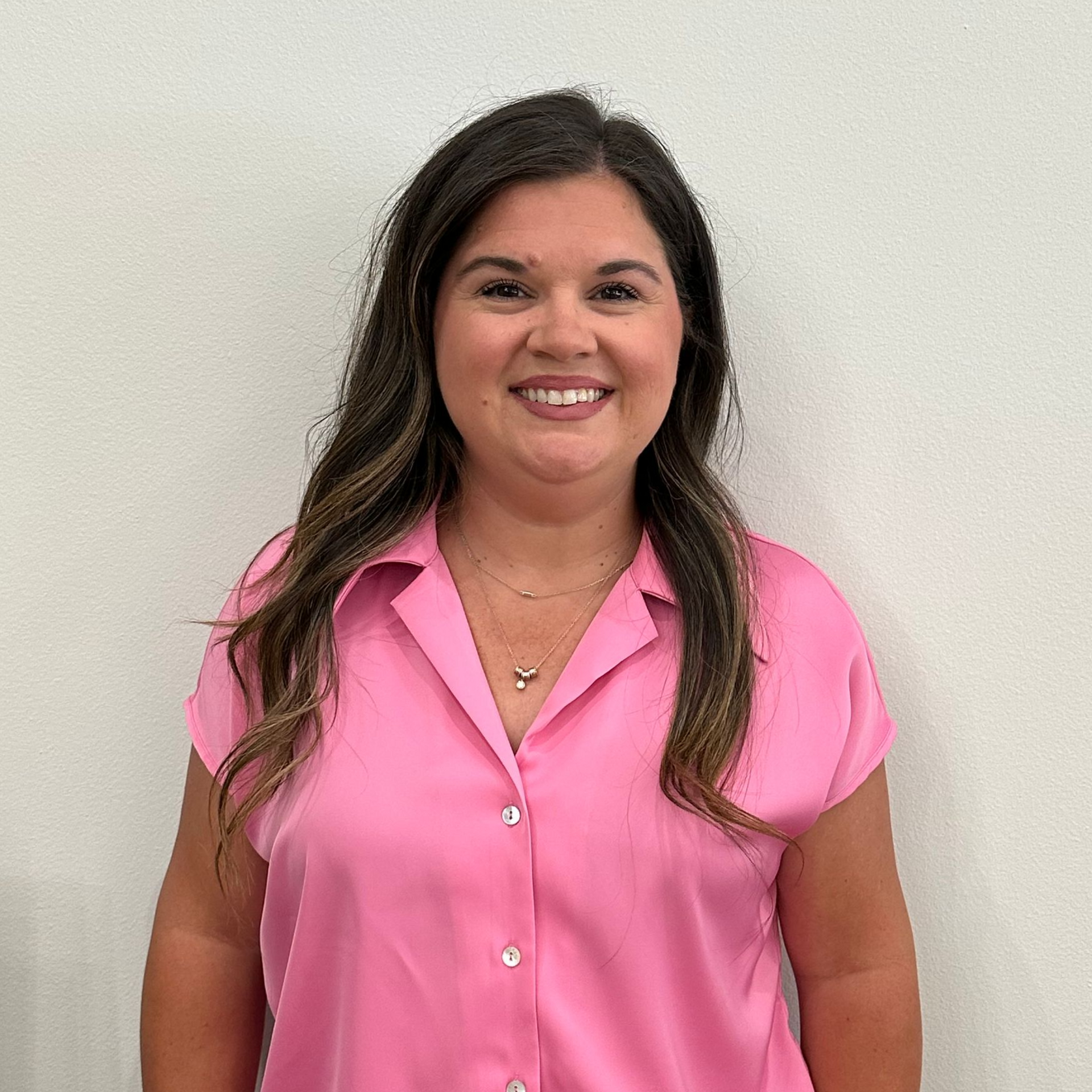 Smiling woman in a pink blouse standing against a plain light background
