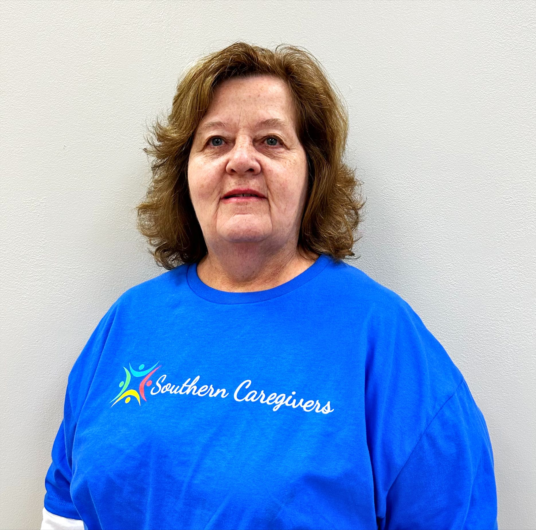 Woman in a blue Southern Caregivers T-shirt against a plain gray wall