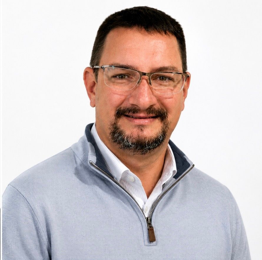 Man standing against a white background, wearing glasses and a striped polo shirt, smiling gently