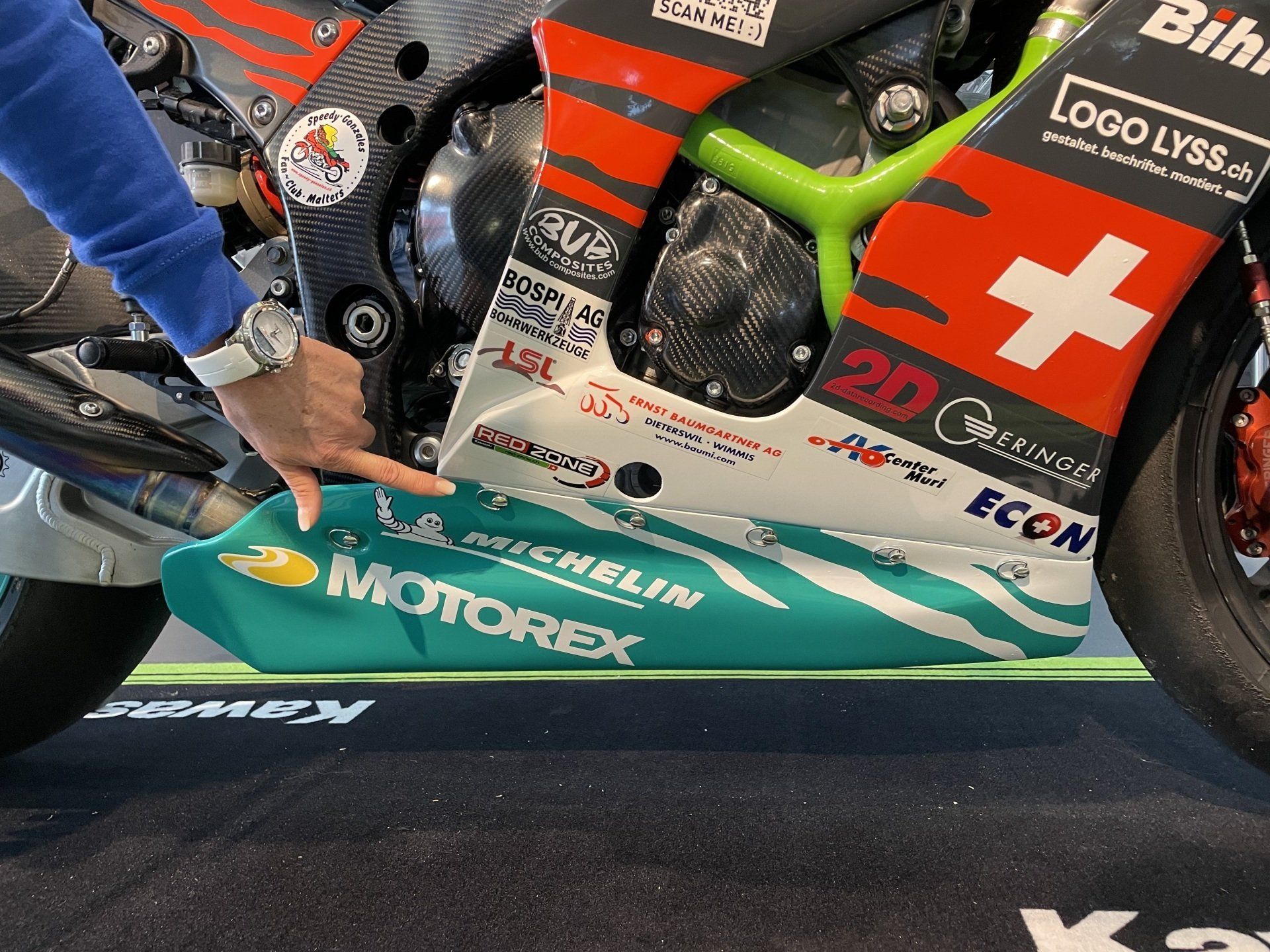 Eine Person zeigt auf die Seite eines Motorrads, auf dem Motorex steht