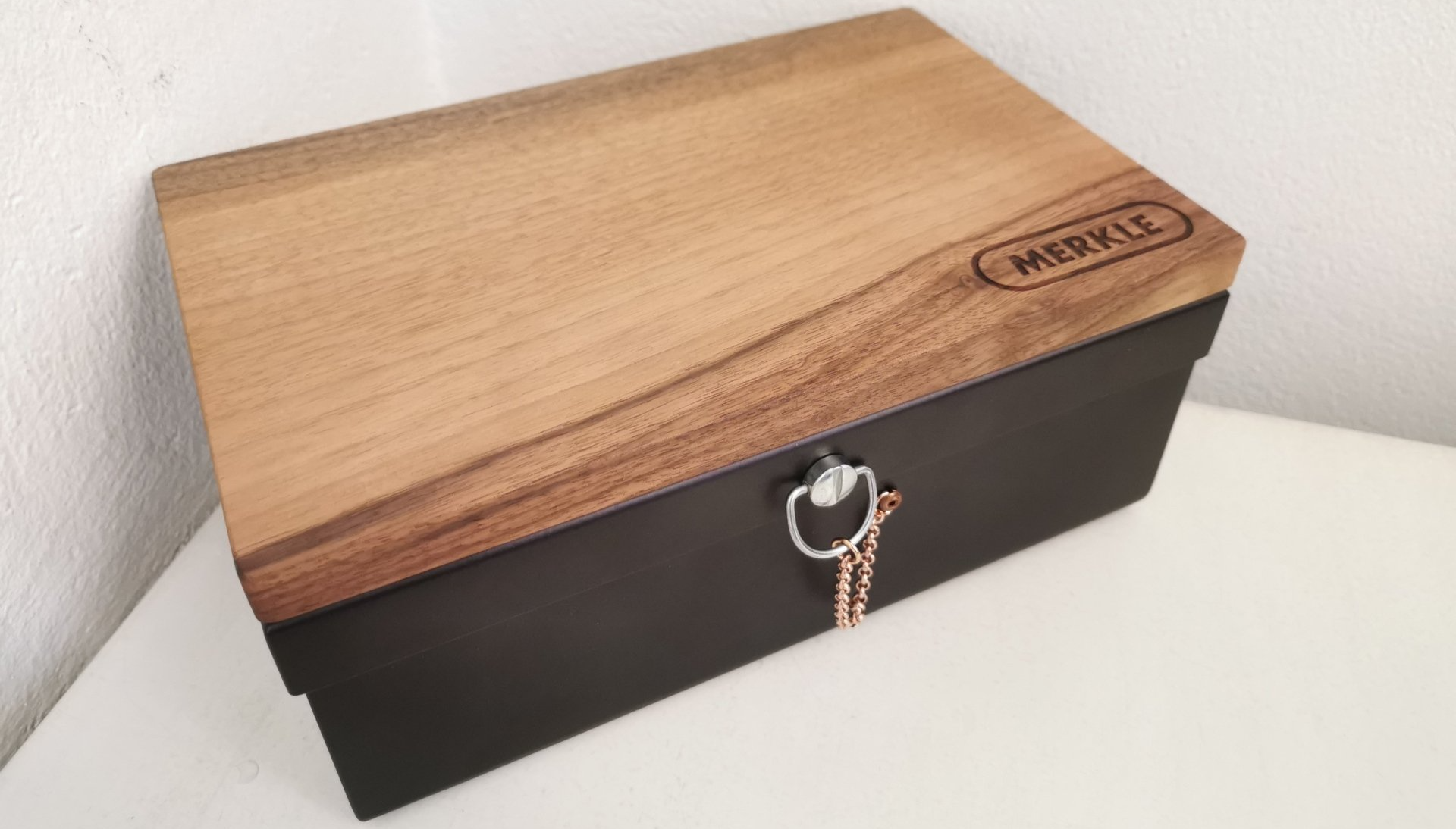 Auf einem weissen Tisch steht eine Holzkiste mit schwarzem Deckel.