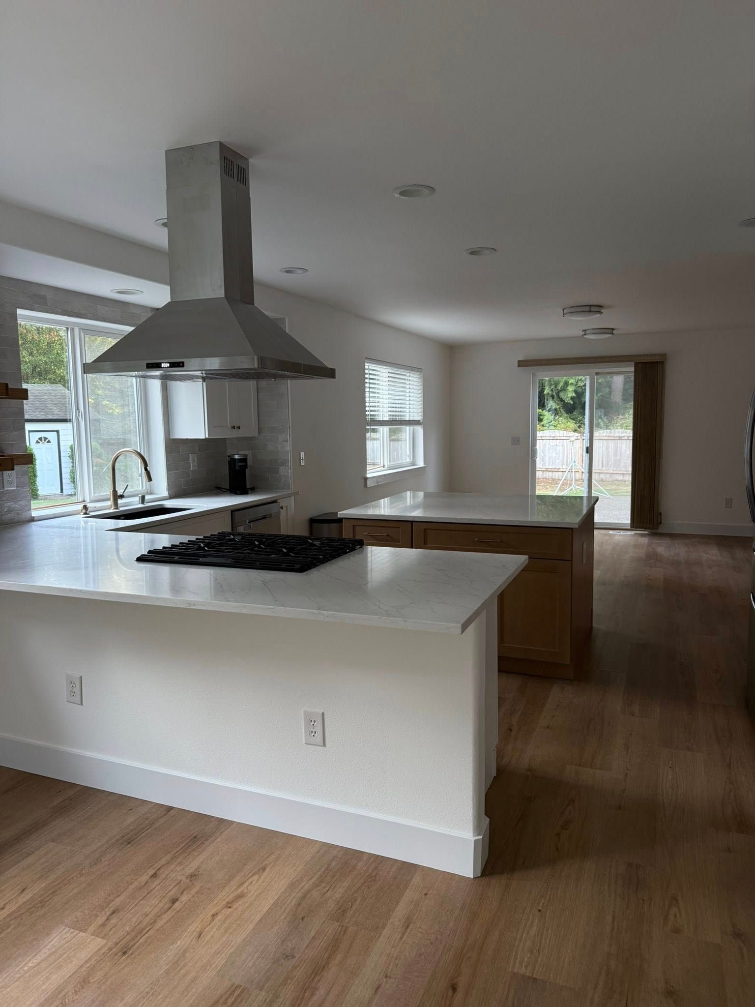 Modern kitchen with two islands, stainless steel range hood, and large windows.