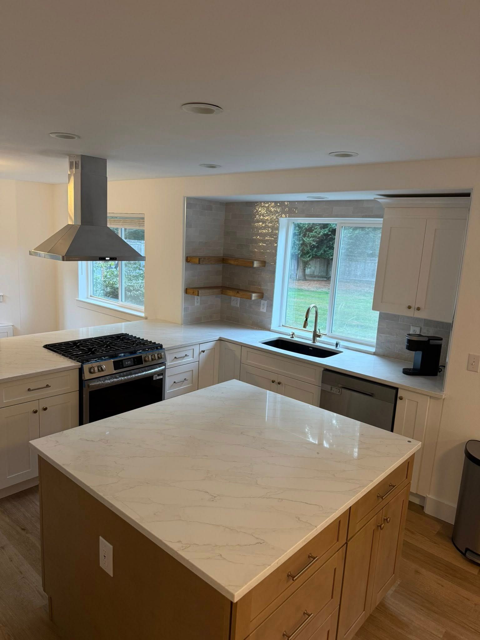 Modern kitchen with white cabinets, marble countertops, stainless steel range hood, and large island.