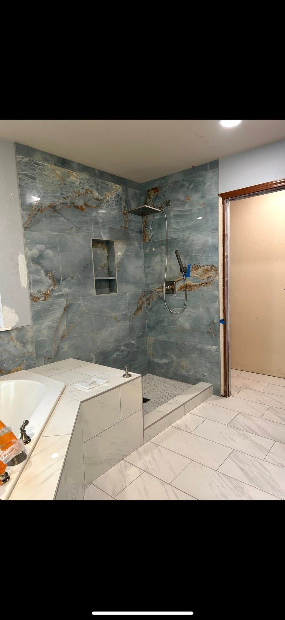 Bathroom with blue marble shower walls, a recessed niche, and white tile floor.