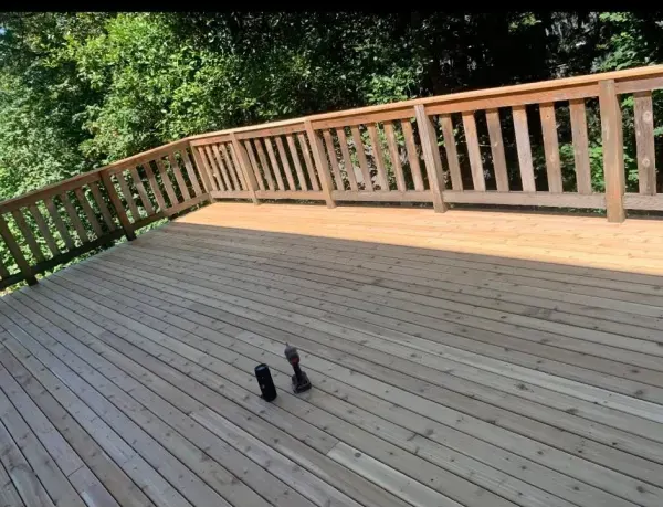 Wooden deck with railing overlooking trees, two tools lie on the deck.