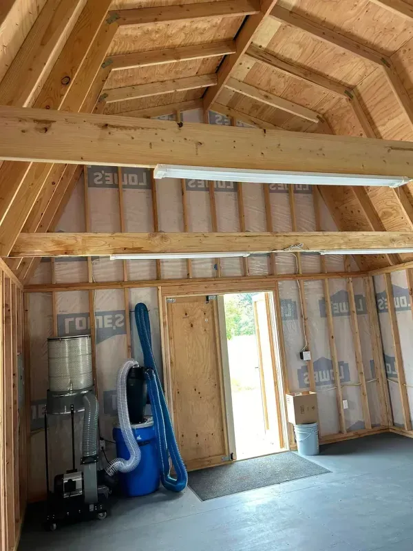 Interior of a new shed with wooden framing, exposed rafters, open door, and tools.