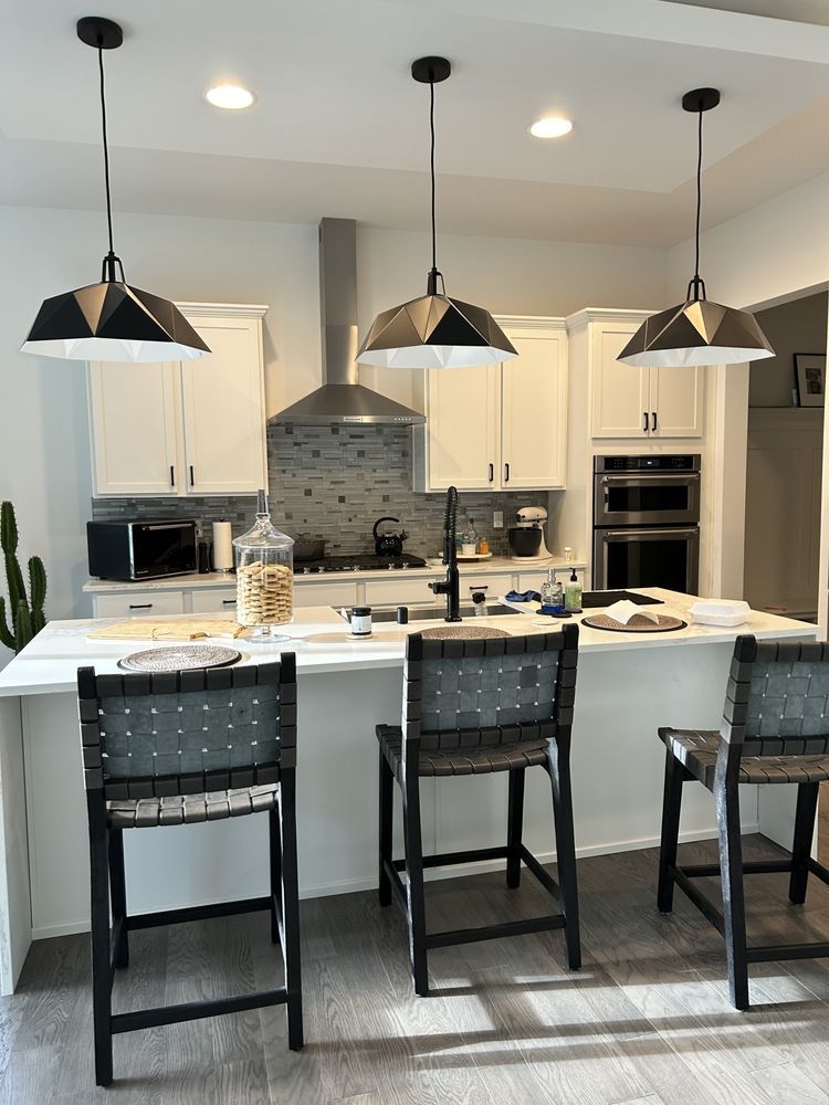 Kitchen with white cabinets, island with stools, and three pendant lights.