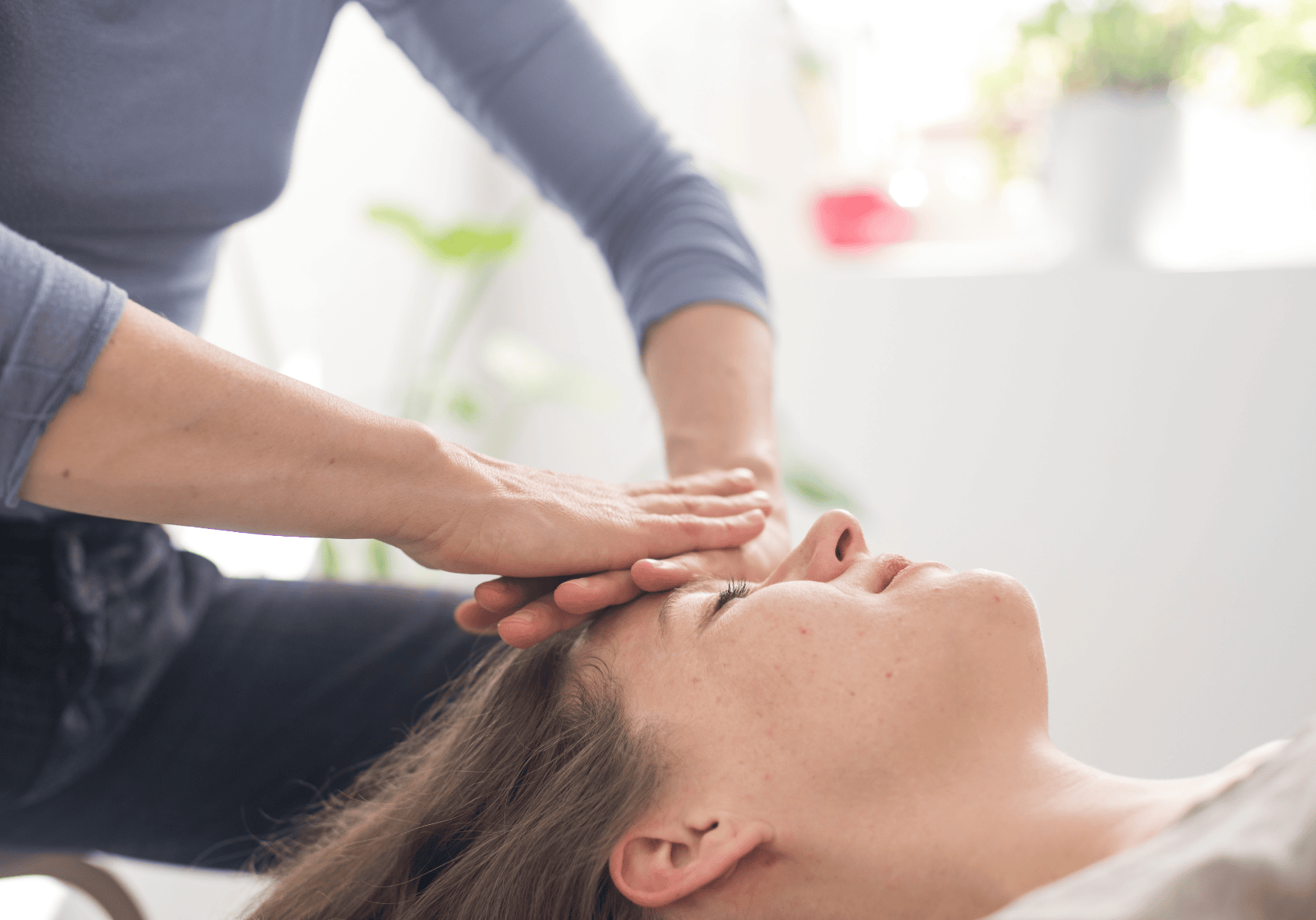 Massage therapist applying a facial treatment to a client lying on a spa bed