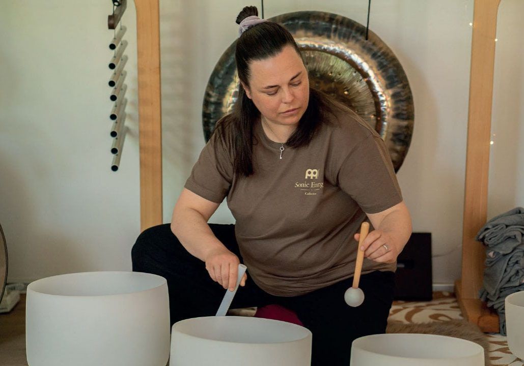 Person playing a white drum in a room with a gong in the background